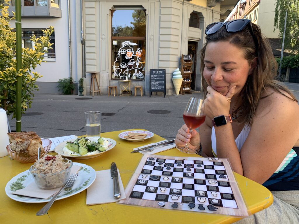 Woman thinking about her next chess move at an outdoor cafe table with appetizers and wine.