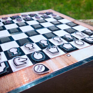 Close up of an open birch wood Travel Chessboard resting on a wooden rail in a park.