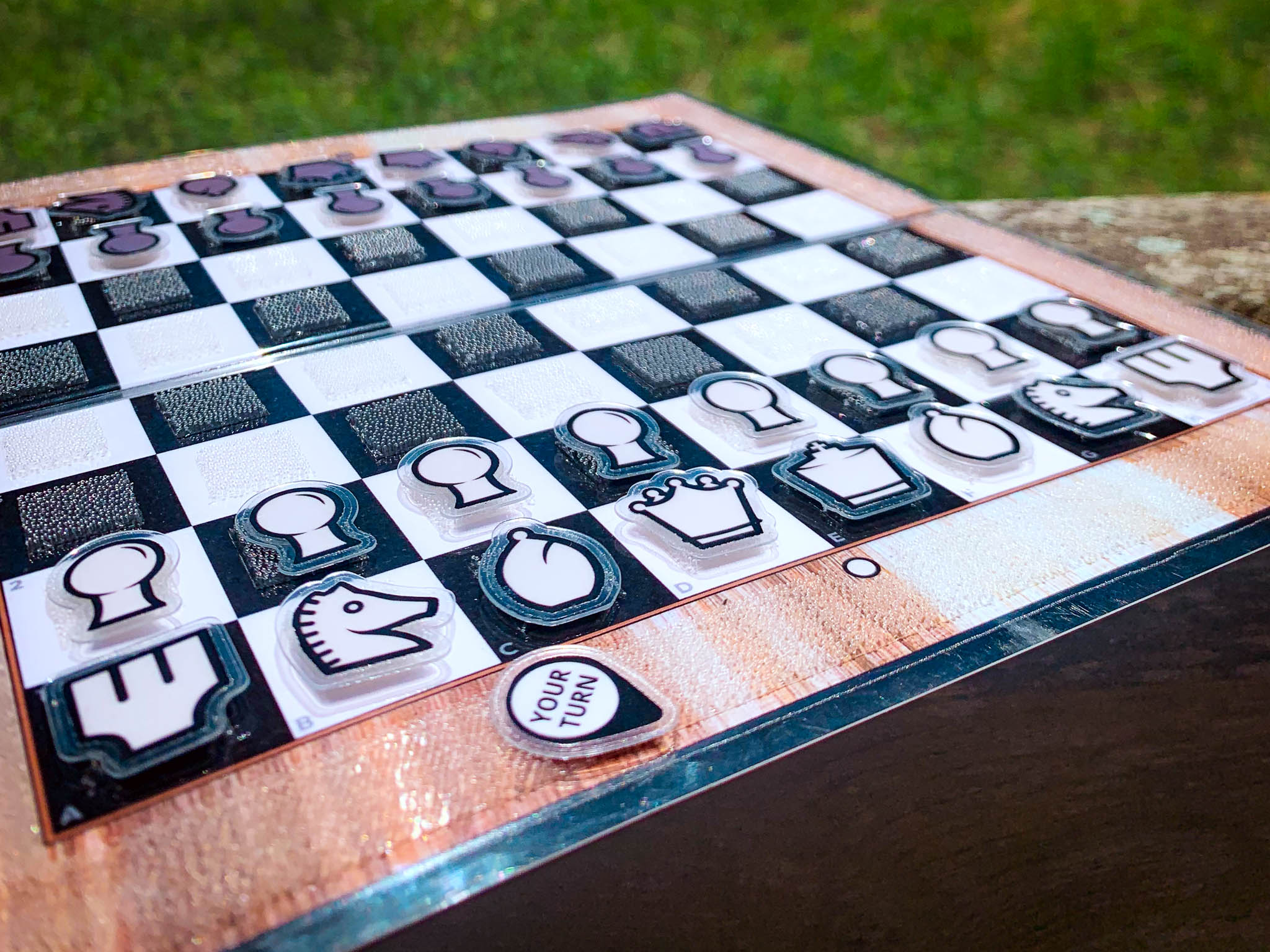 Close up of an open birch wood Travel Chessboard resting on a wooden rail in a park.