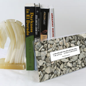 Closed Travel Chessboard with rocks, leaning against a few books buttressed by a marble knight bookend, all on a white background.